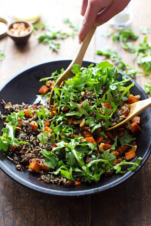 Roasted Sweet Potato, Wild Rice, and Arugula Salad in a bowl with wooden spoons.