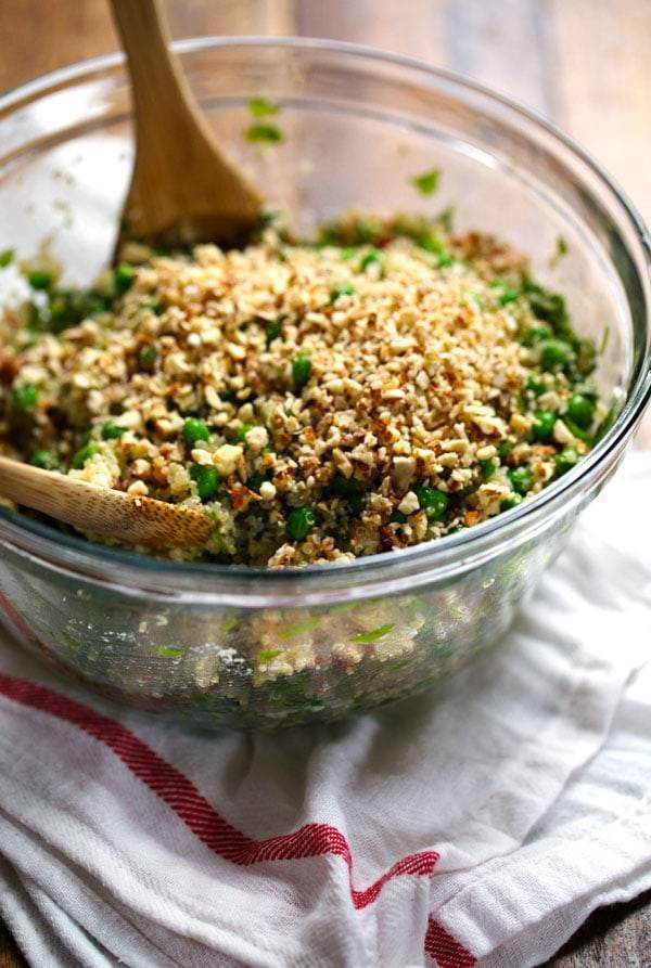 Quinoa Salad in a clear mixing bowl with two wooden spoons.