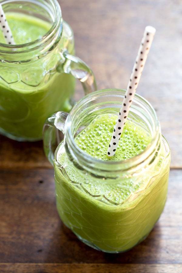 Two green smoothies in jars with straws.