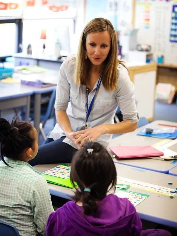 A teacher in the classroom talking to two students.