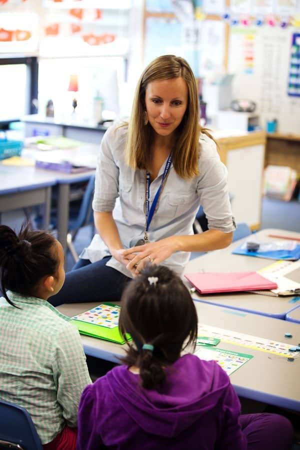 A teacher in the classroom talking to two students.