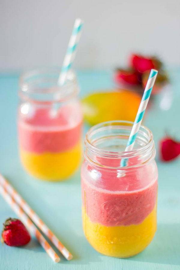 Pink and yellow smoothies in jars with straws.