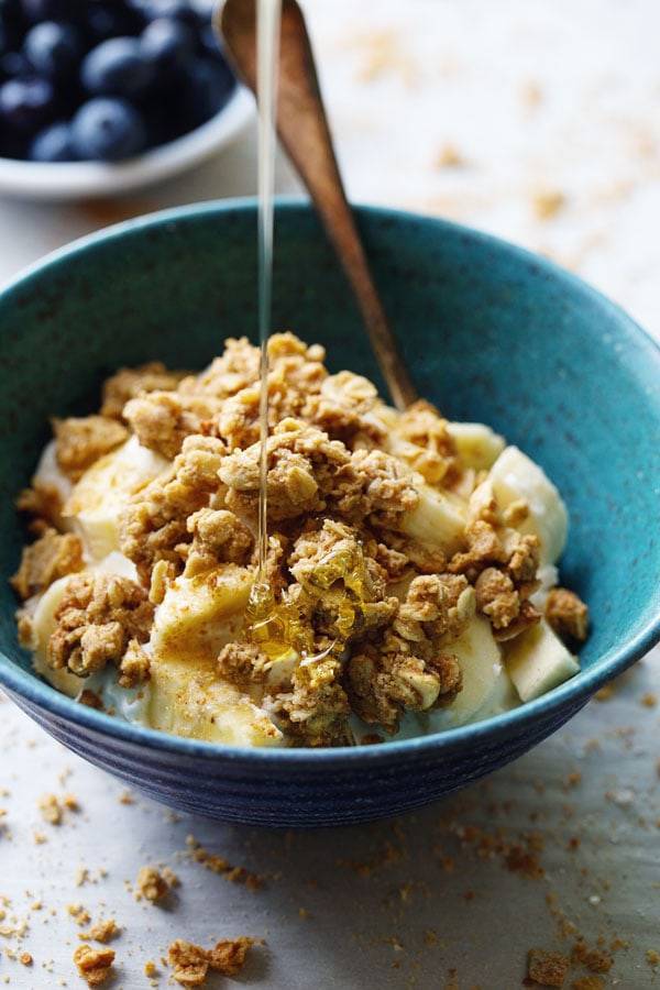 Granola over bananas with honey drizzle in a blue bowl.