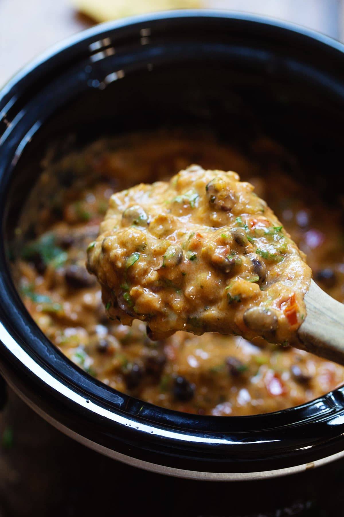 Cheesy Chili Dip in a slow cooker and on a wooden spoon.