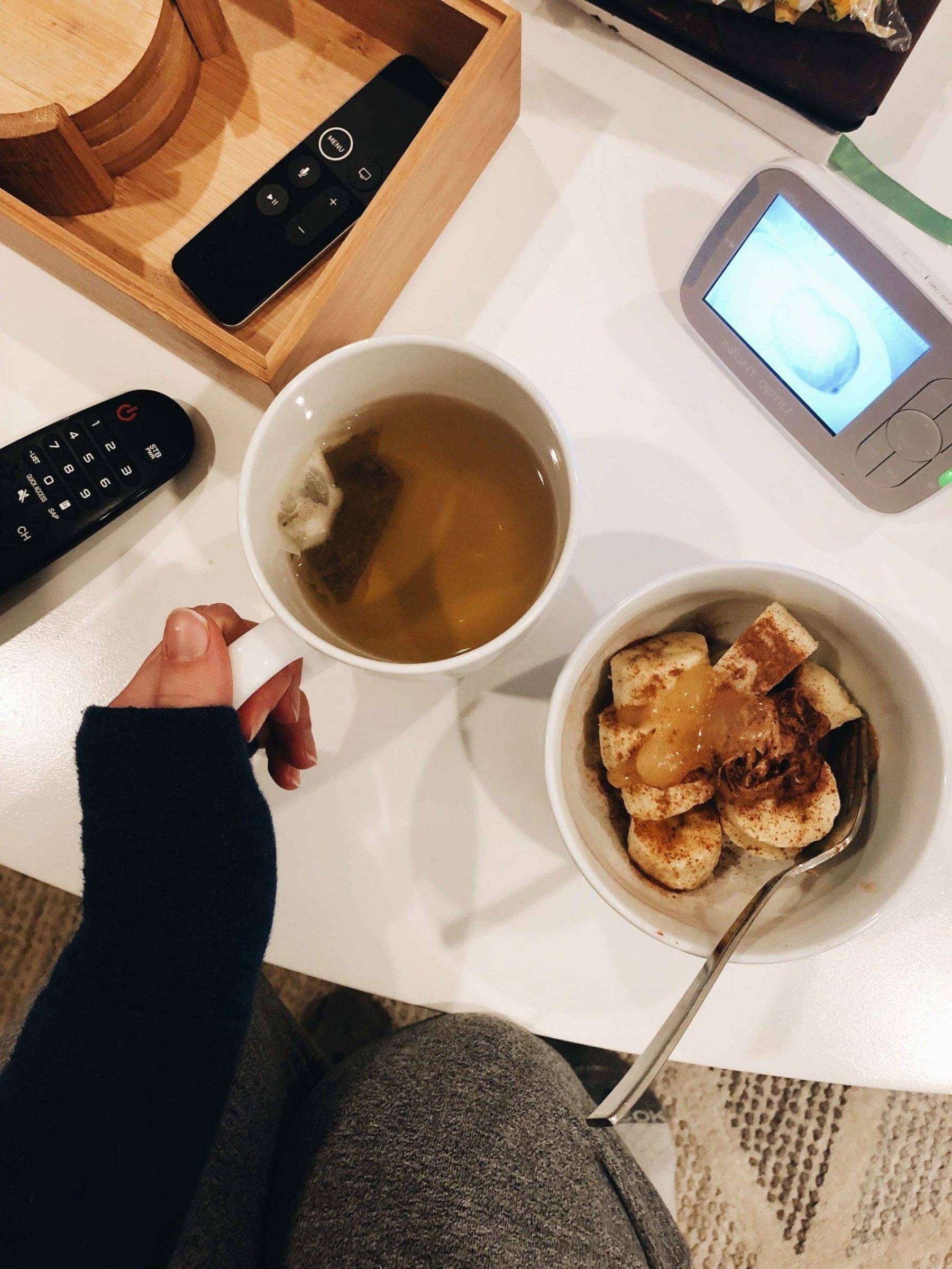 A counter with remotes, tea, a bowl of bananas, and a baby monitor.