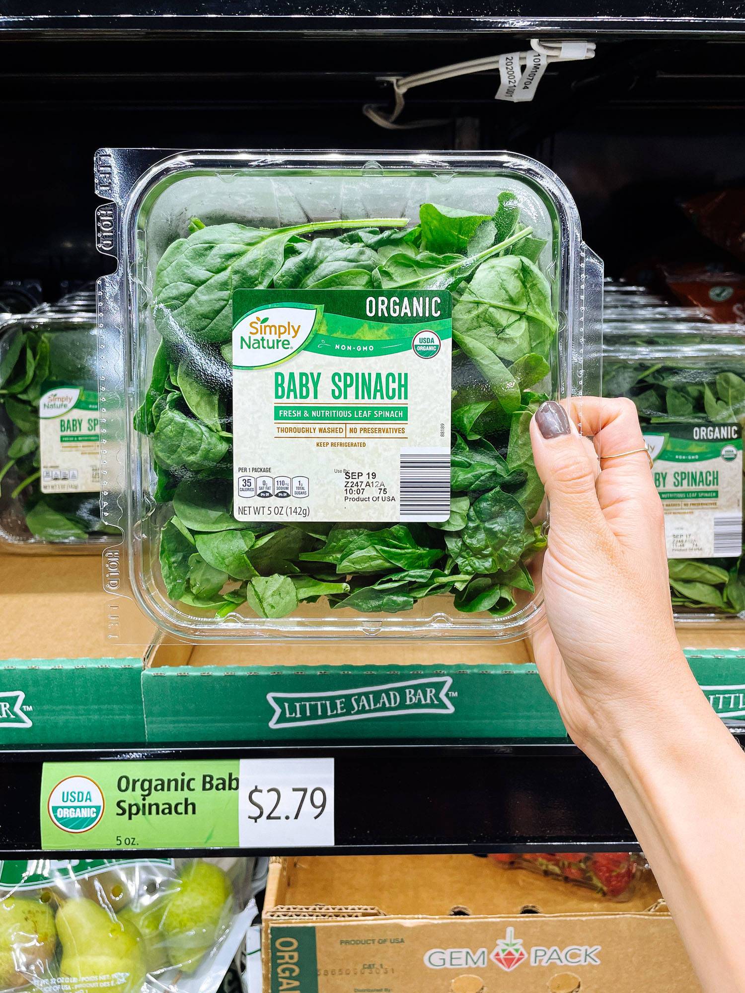 White hand holding a container of spinach from ALDI.