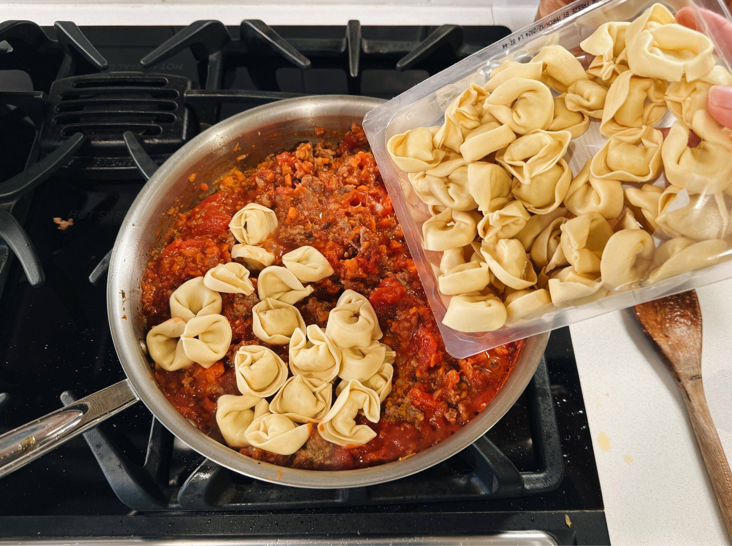 Adding tortellini and tomato sauce to the pan