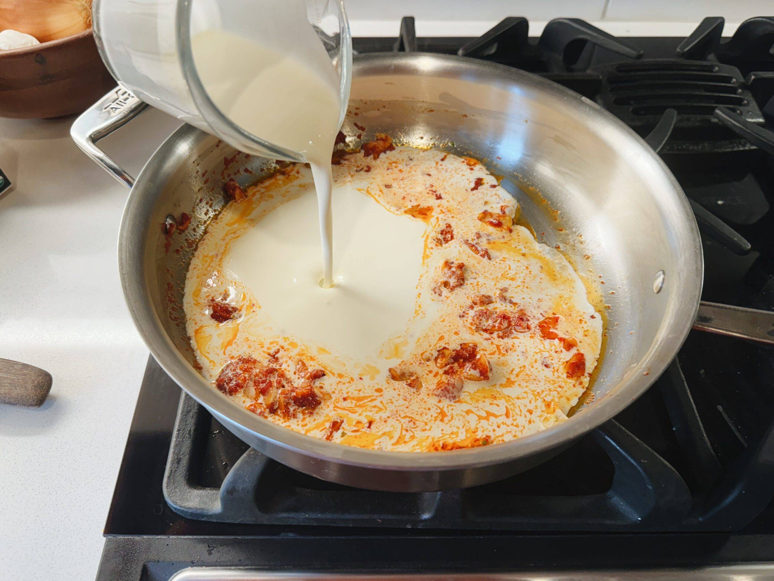 Pouring heavy cream into a pan with tomatoes.