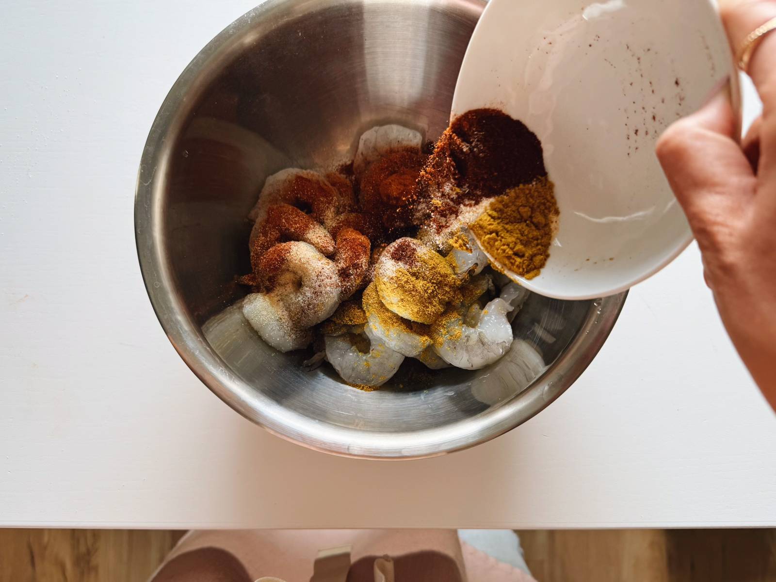 Pouring spices on raw shrimp in a bowl.