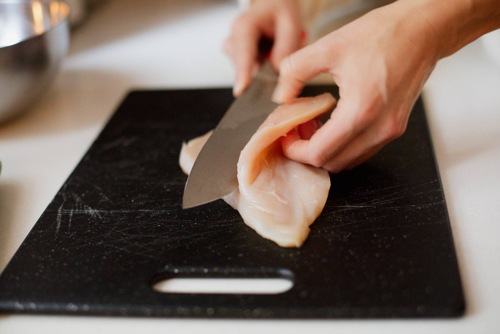 Slicing chicken breasts in half with a knife.