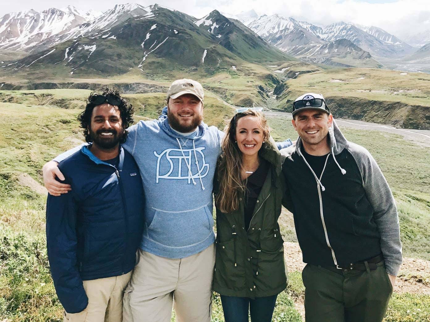Four people smiling in front of mountains.