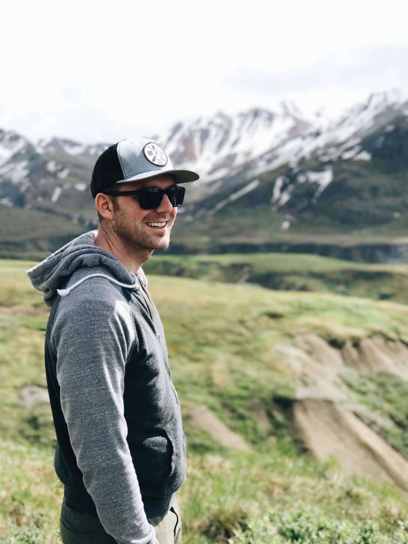 Man smiling with sunglasses in front of mountains.