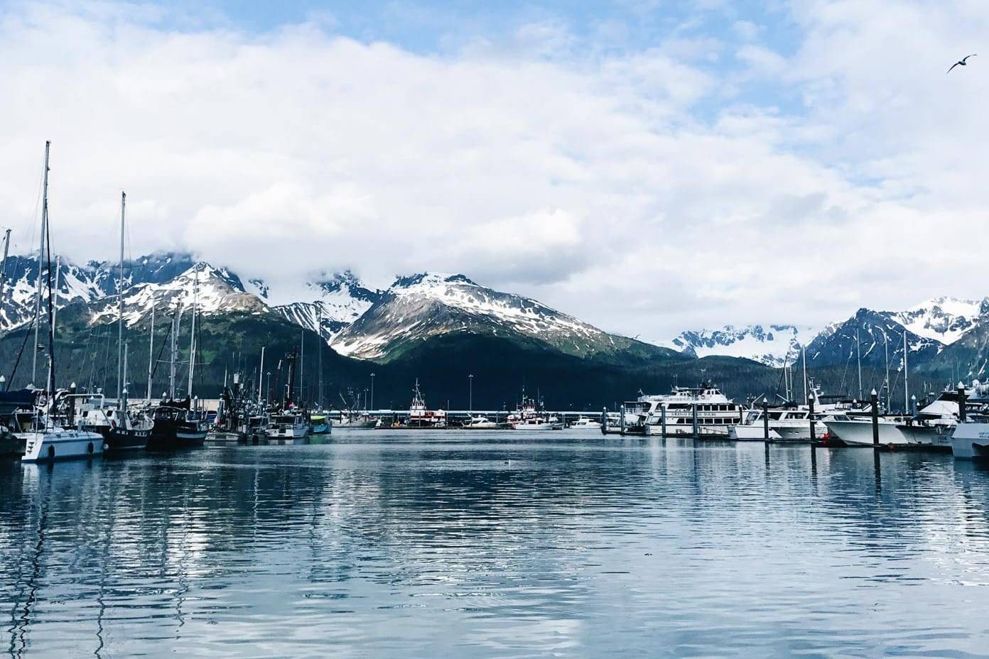 A calm lake at a luxury yacht dock nestled in a valley surrounded by snow-capped mountains.