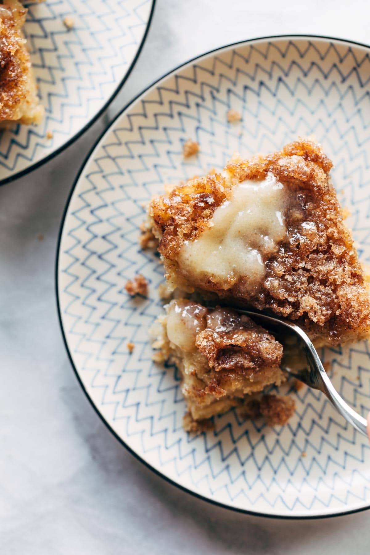 A plate holding a piece of Cinnamon Sugar Apple cake with a piece cut by a fork.