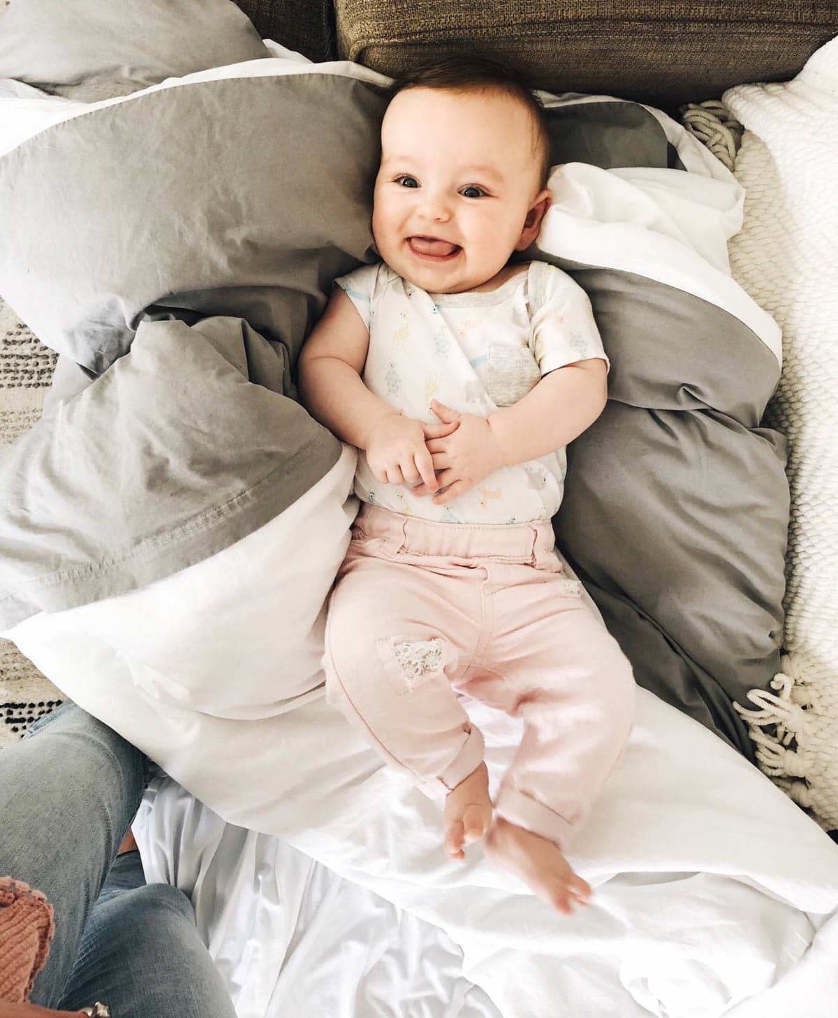 A smiling baby lying in pillows on a bed.