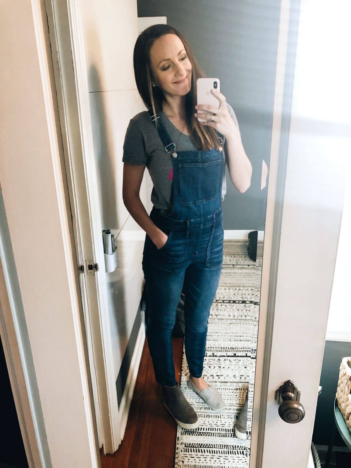 A lady with overalls smiling and taking a selfie.