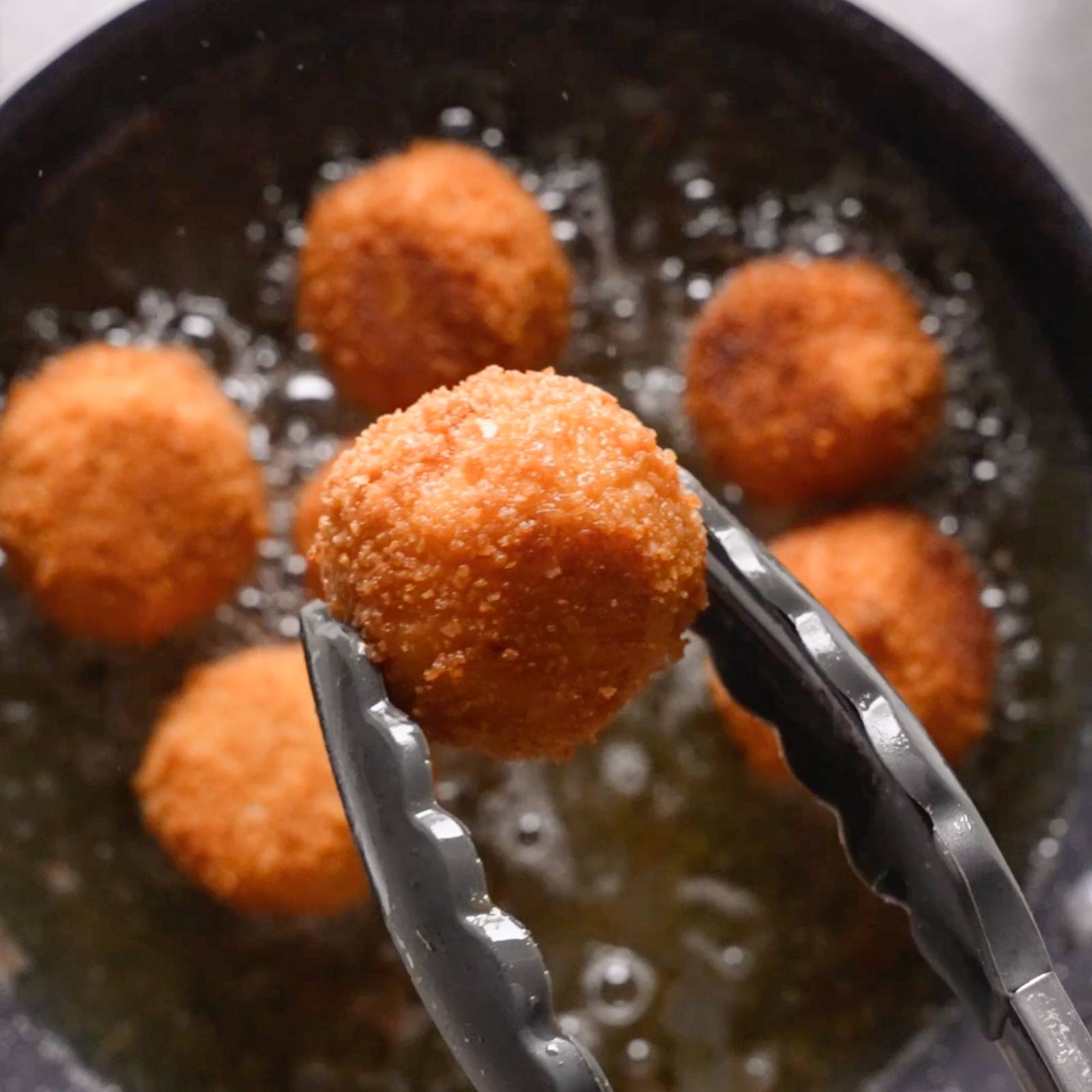 Tongs holding a ball of fried arancini.