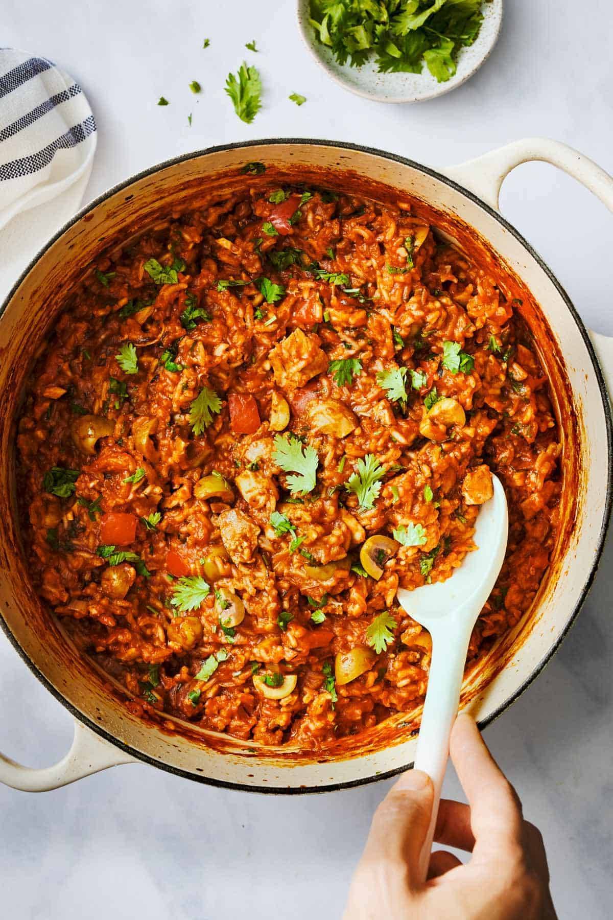 Arroz Con Pollo in a dutch oven with a serving spoon.