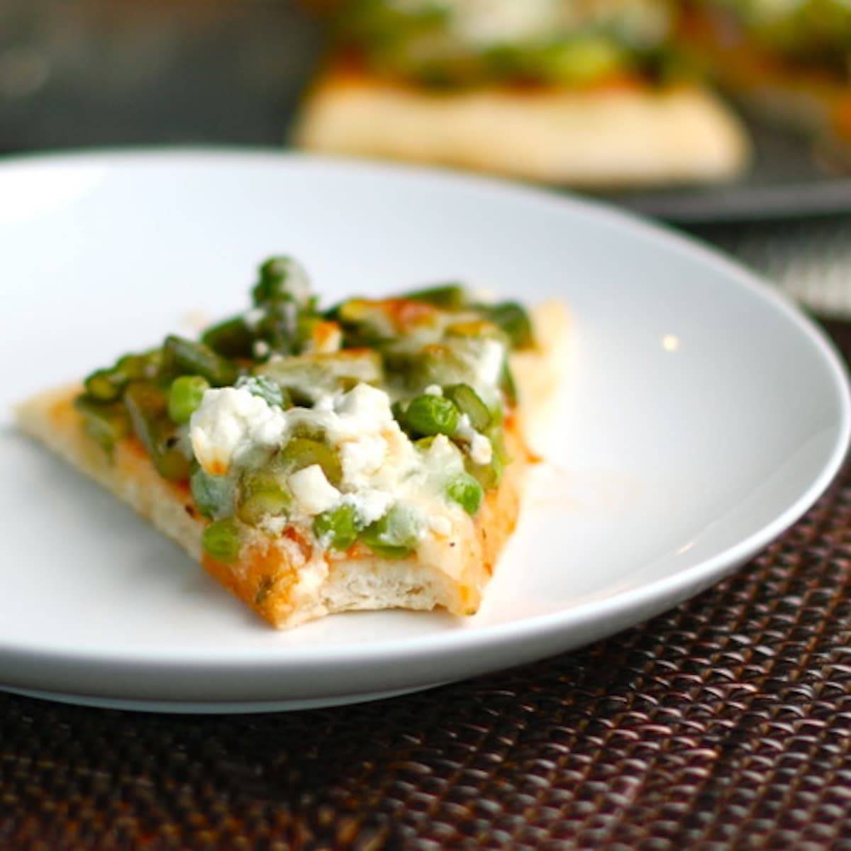 Asparagus, peas, and goat cheese pizza on a white plate.