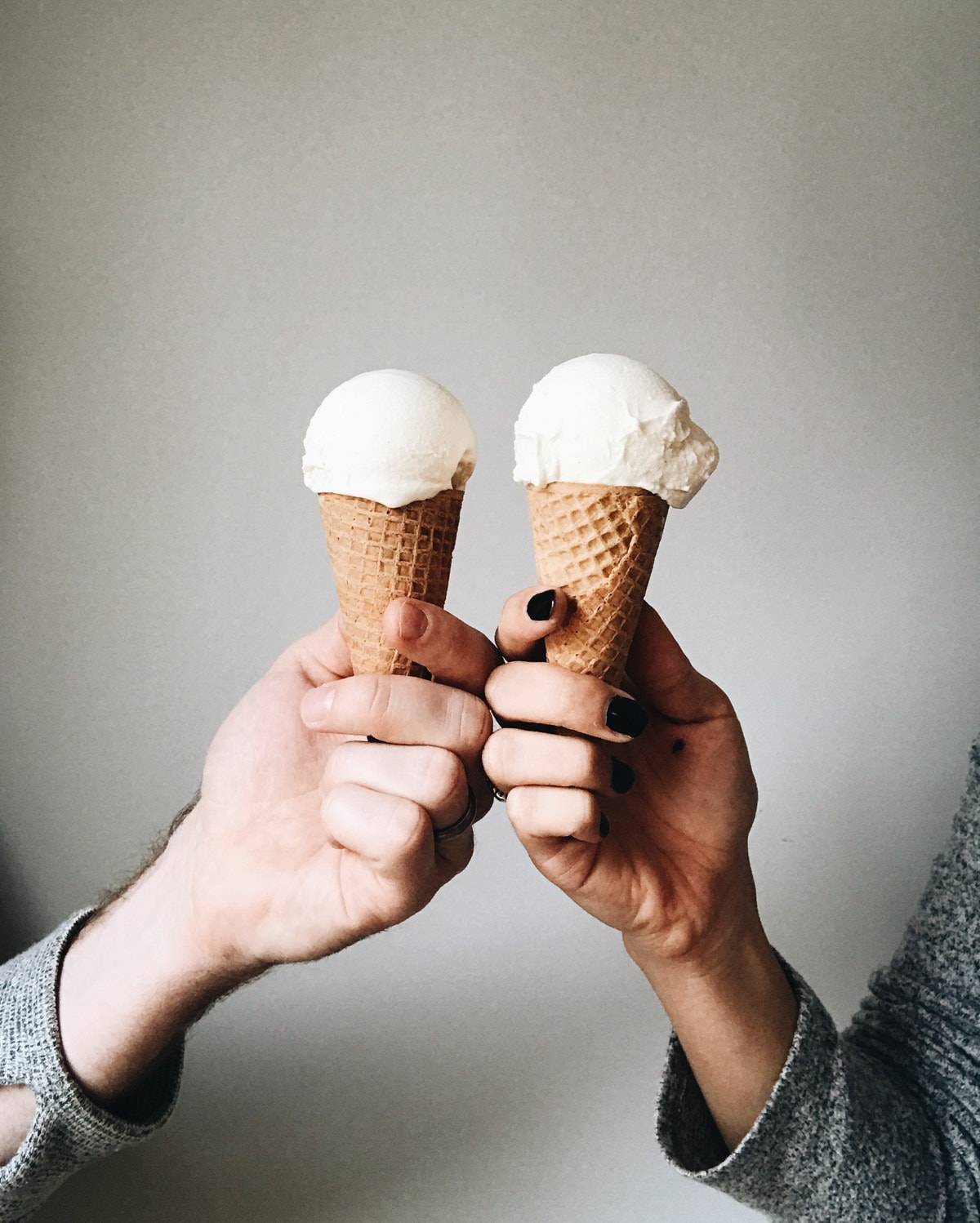Two hands holding two ice cream cones.