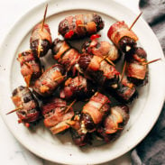 Bacon-wrapped dates on a plate with toothpicks in the dates.