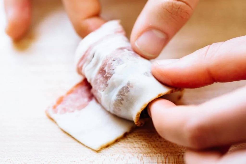 Wrapping bacon around a cheese-stuffed date.