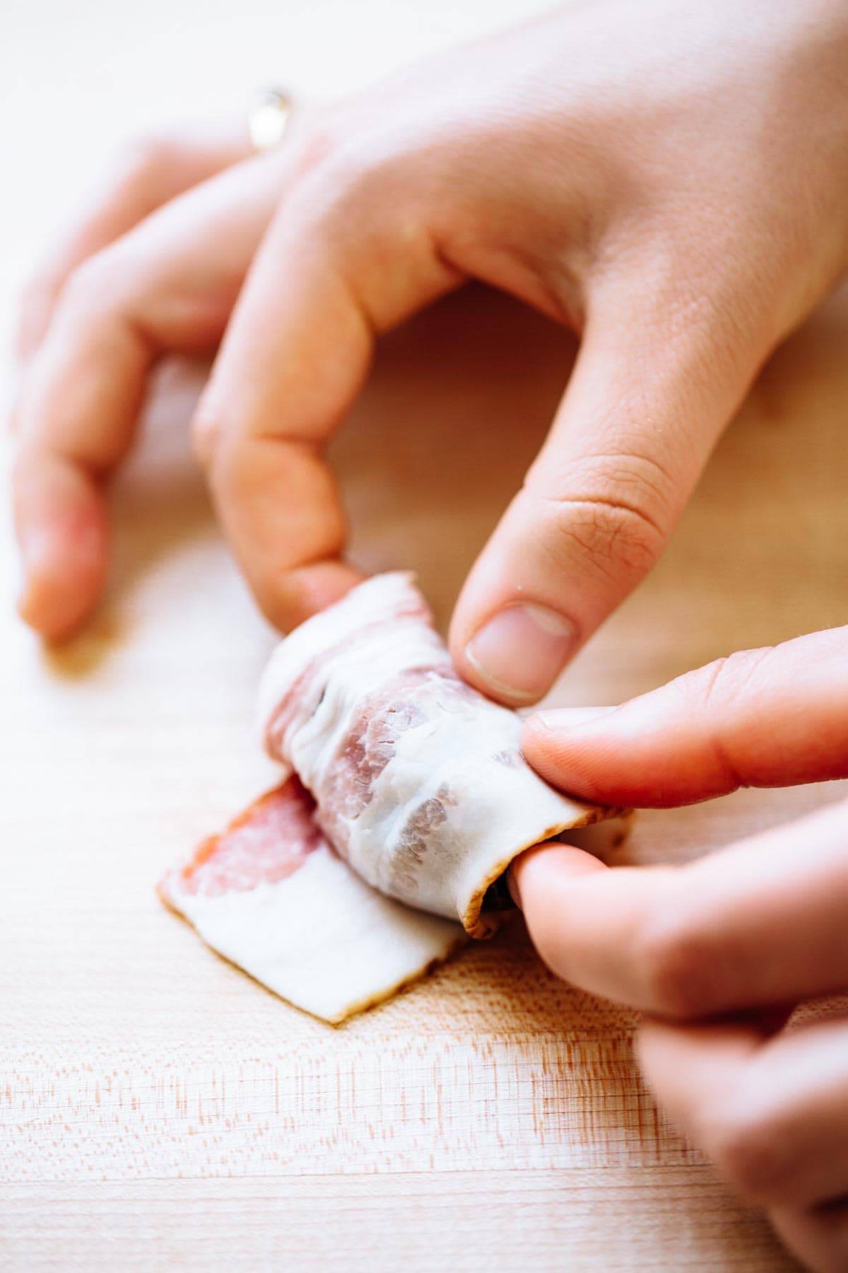 White hand wrapping bacon around a date. 