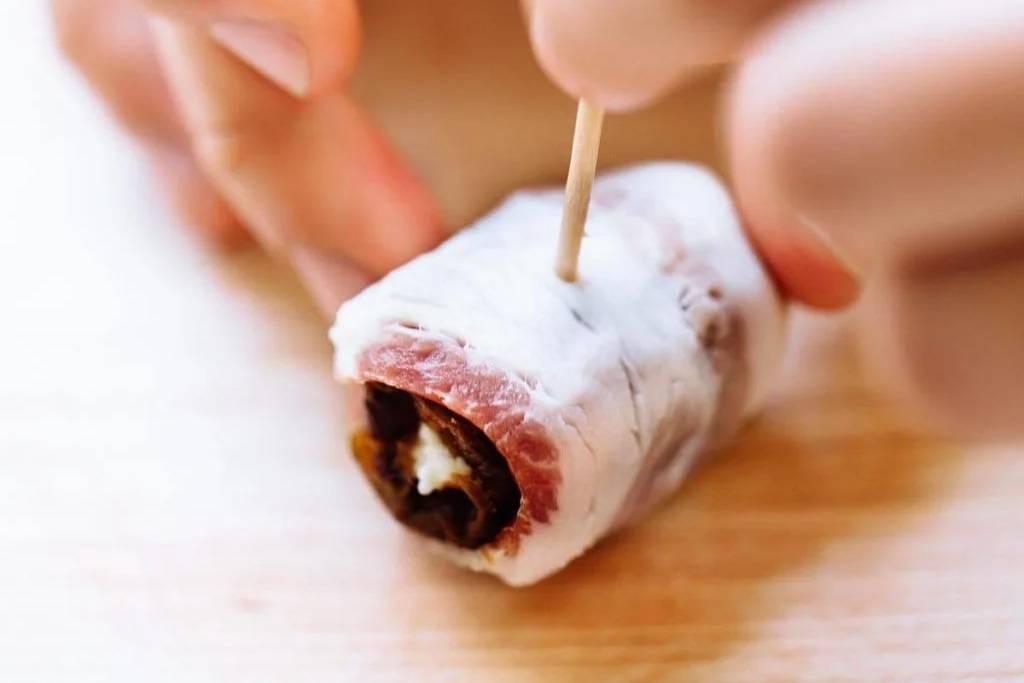 Sticking a toothpick in a bacon-wrapped date.