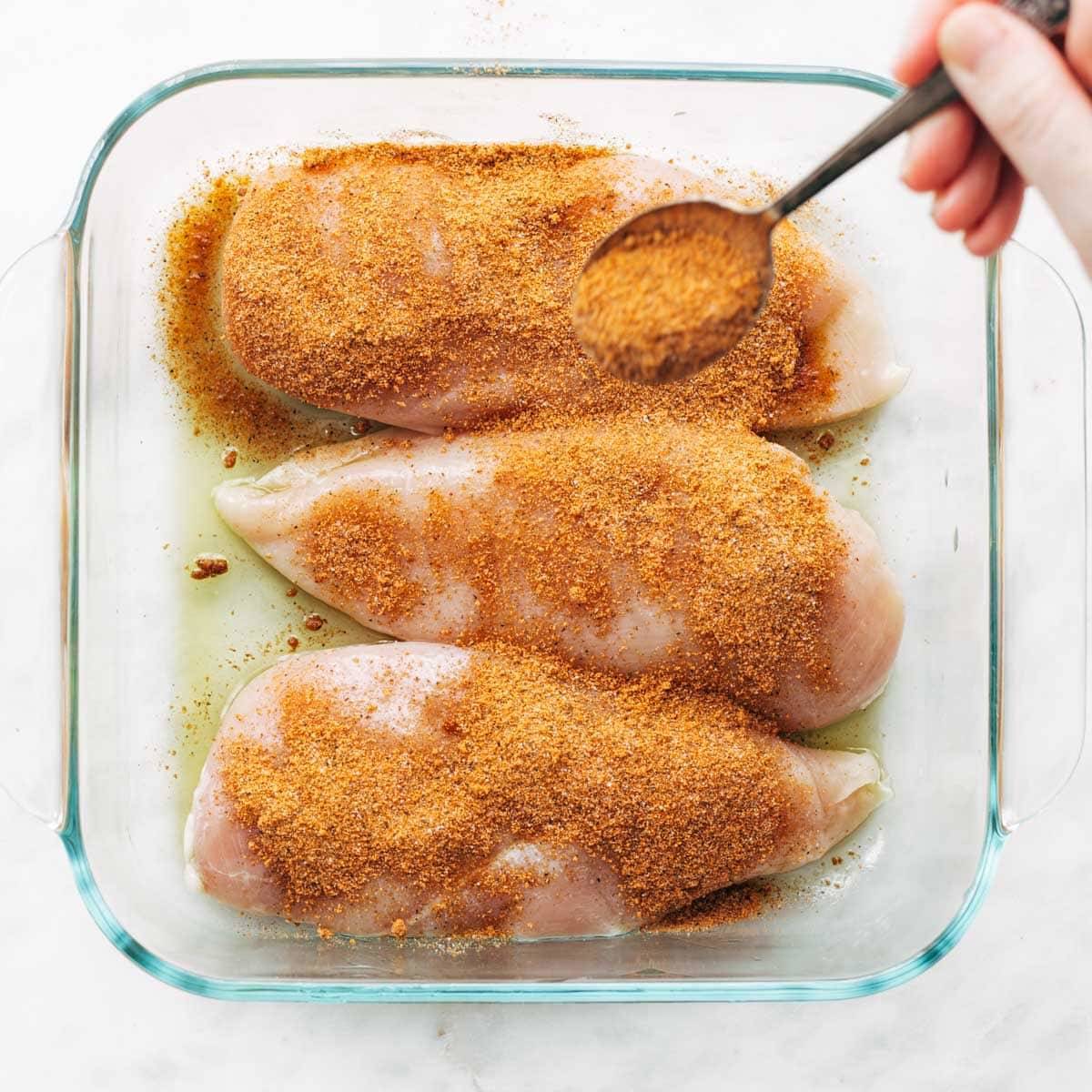 Adding seasoning to chicken breasts.