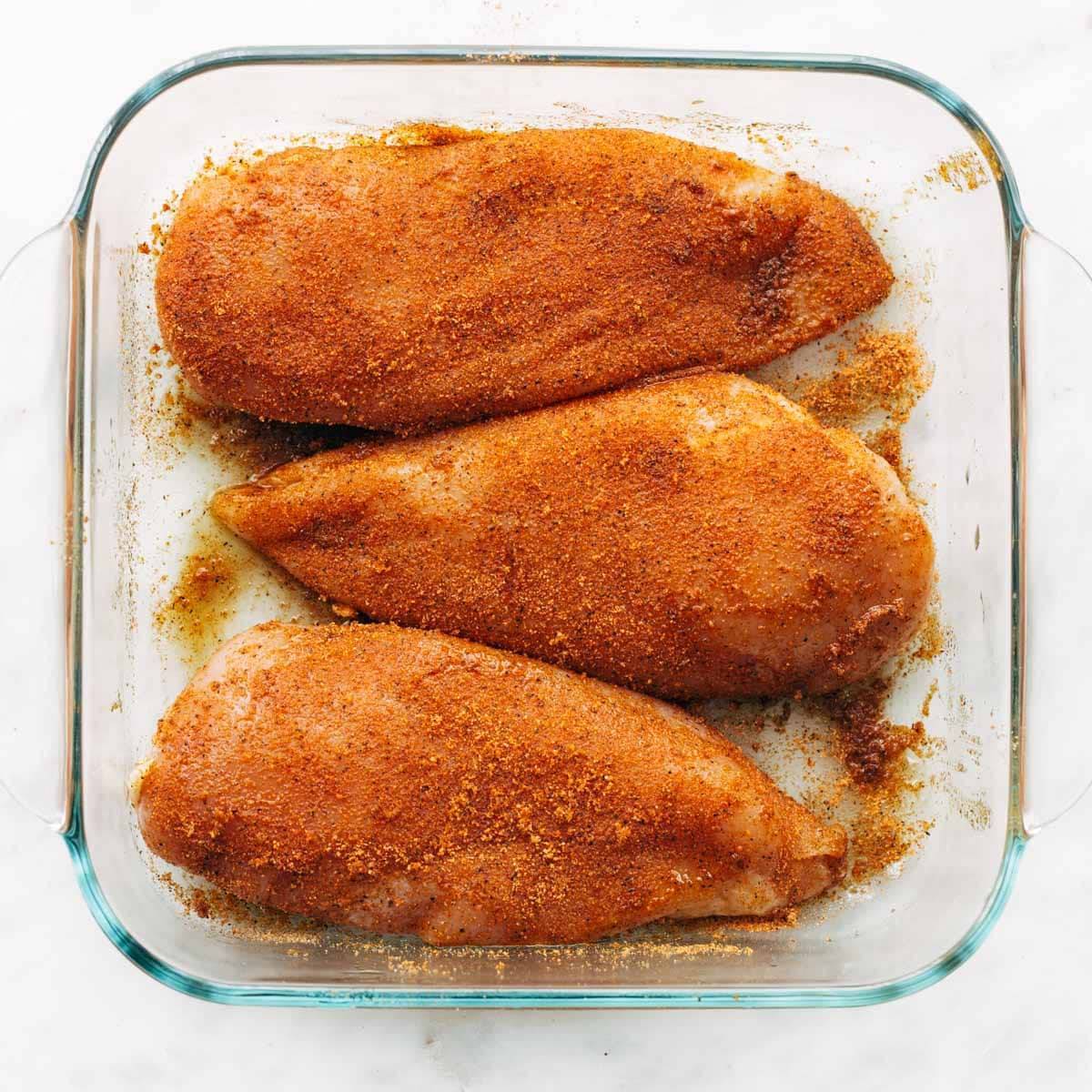 Seasoned chicken breasts in a pan.