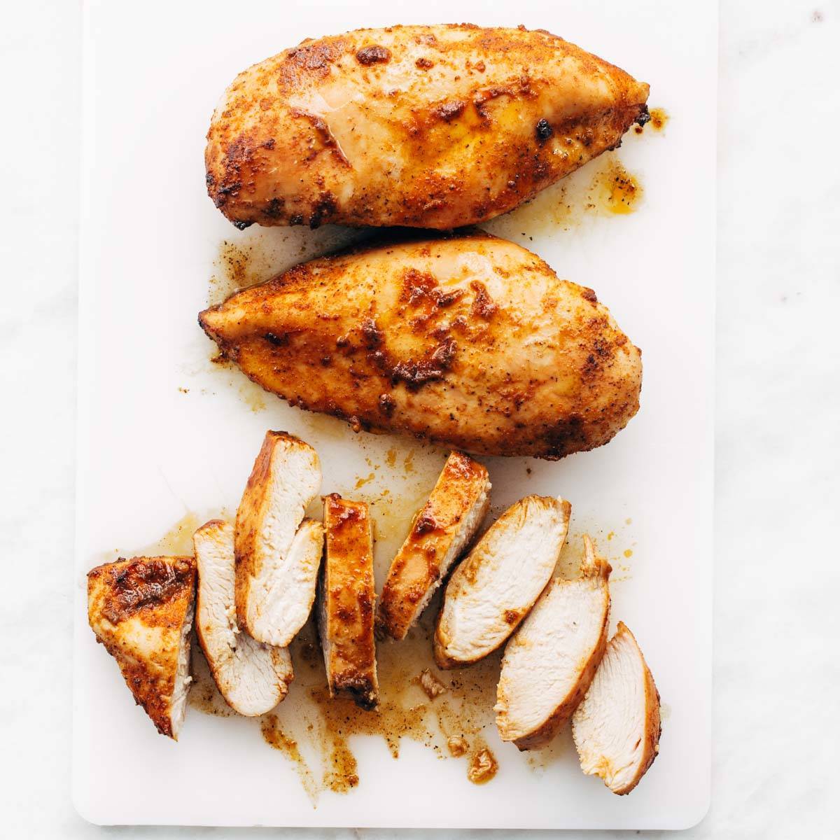 Baked chicken breasts sliced on a cutting board.