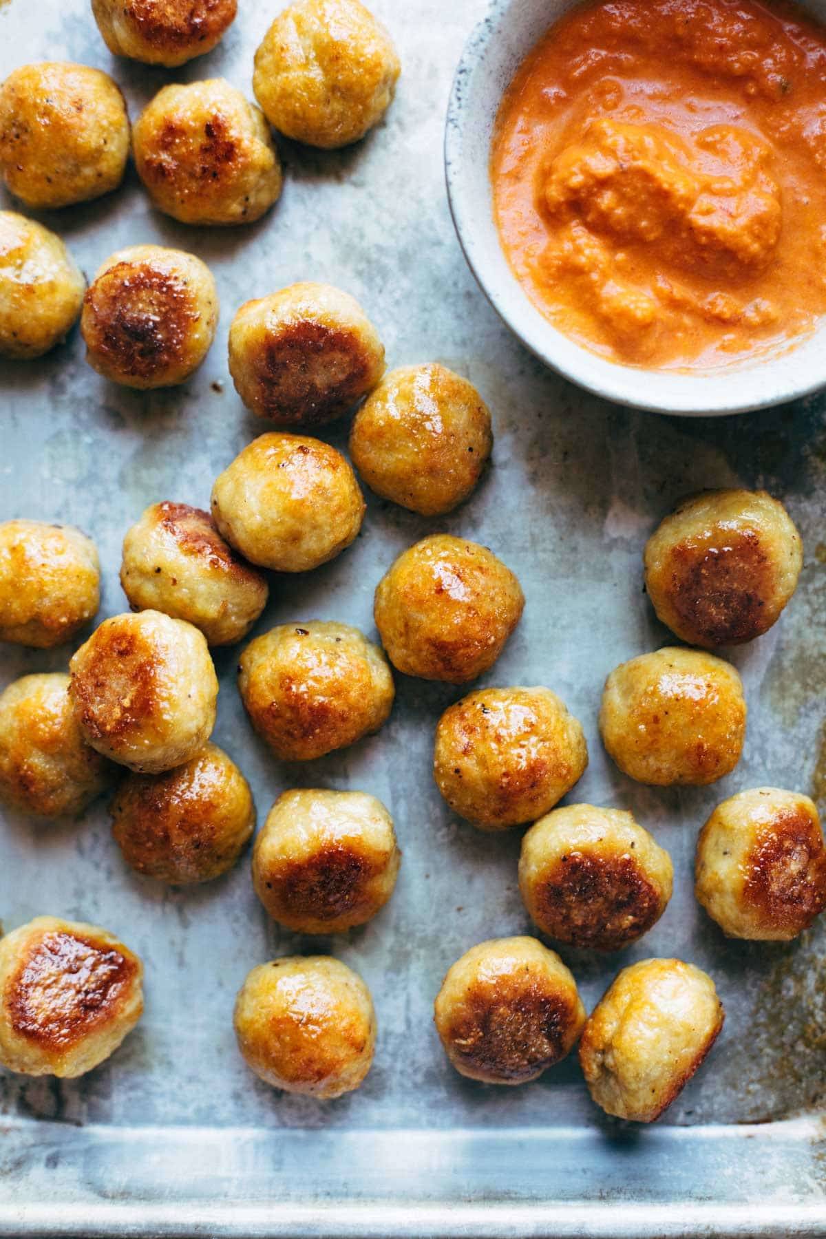 Chicken meatballs next to a bowl of dipping sauce.