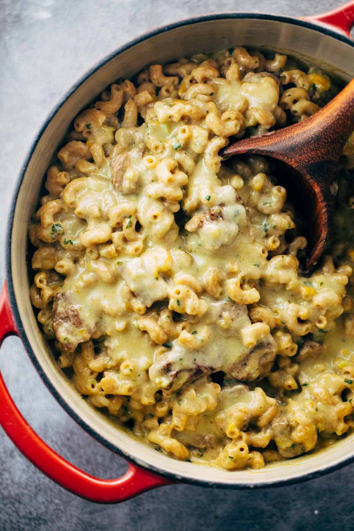 Steak and Cheddar Mac and Cheese in a dutch oven with a wooden spoon.