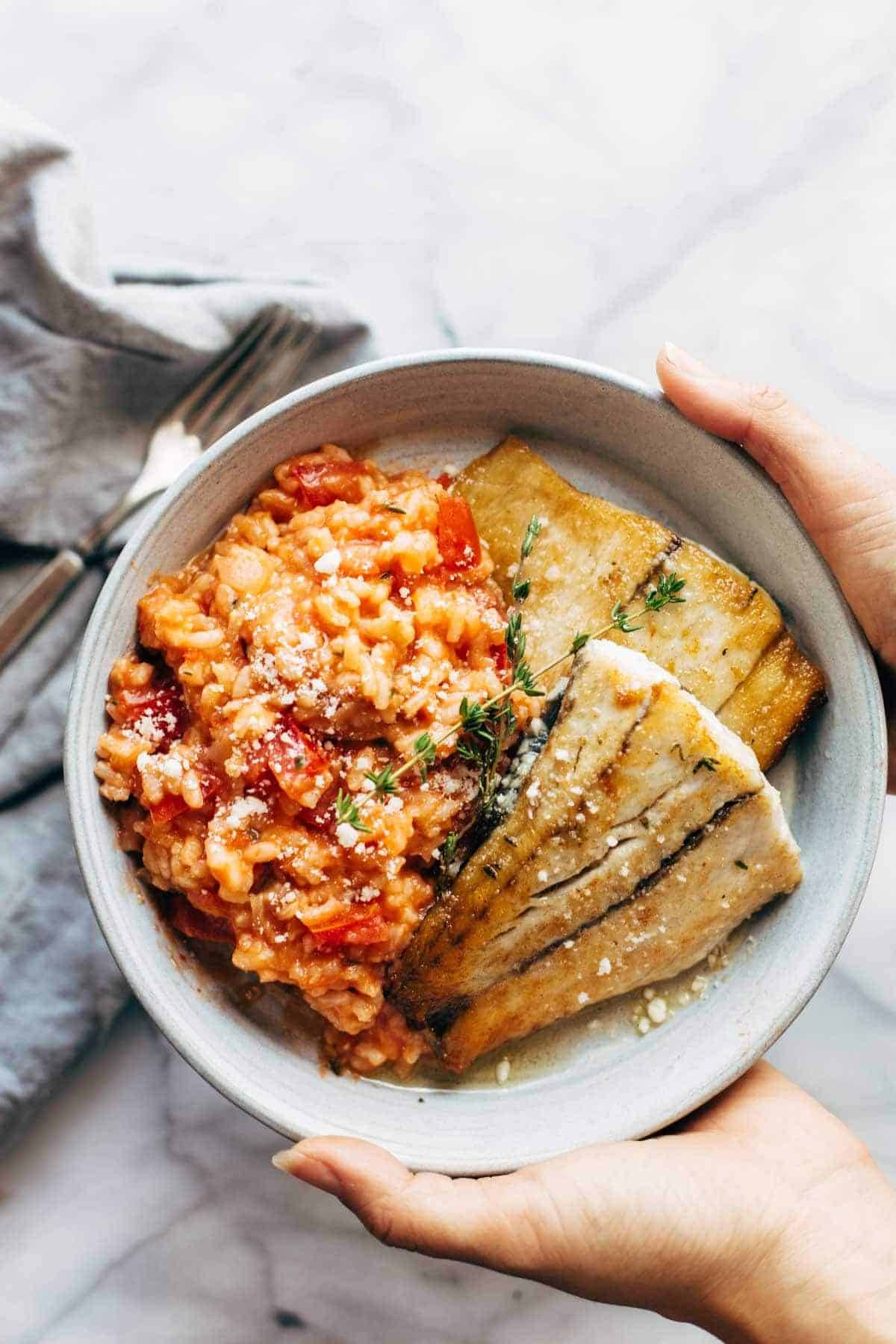 Hands Holding a plate of Creamy Tomato Risotto with Pan Fried Barramundi