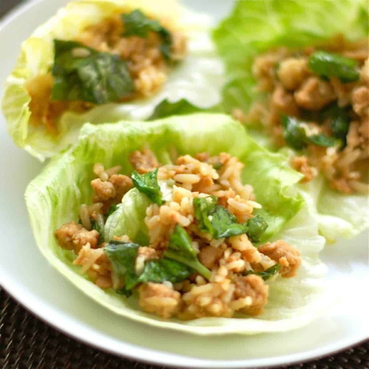 Three basil chicken lettuce wraps on a white plate.