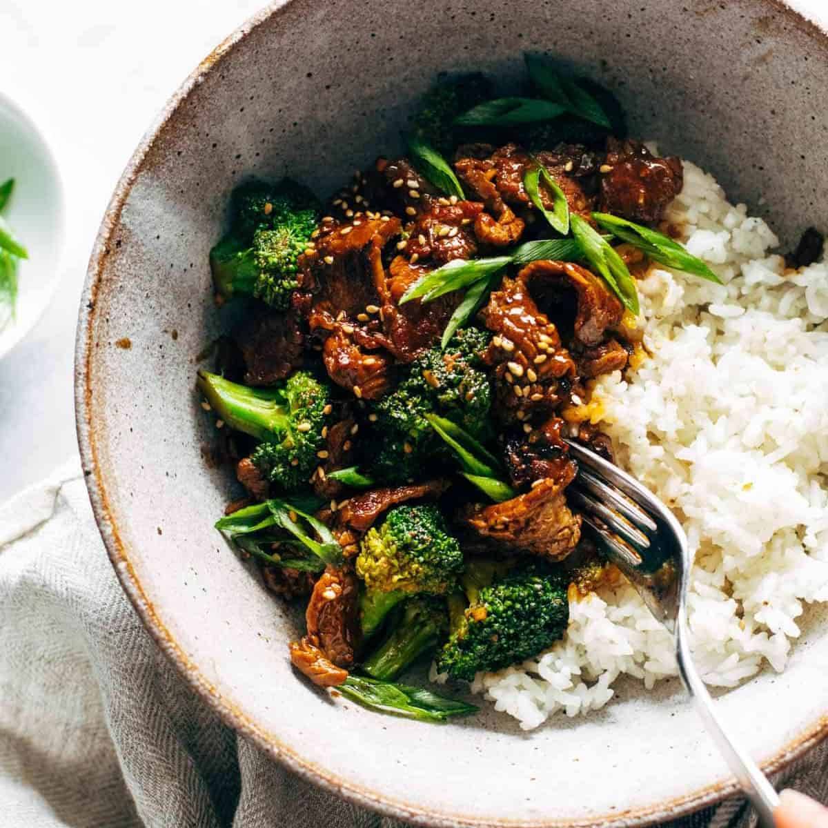 Hearty, saucy beef and broccoli with a side of white rice, and green onions in a rustic bowl.
