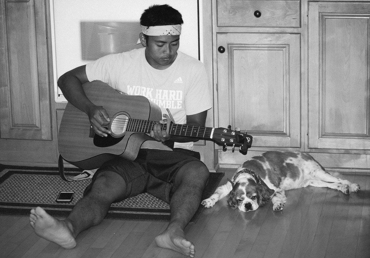 Boy playing guitar on the floor with a dog.