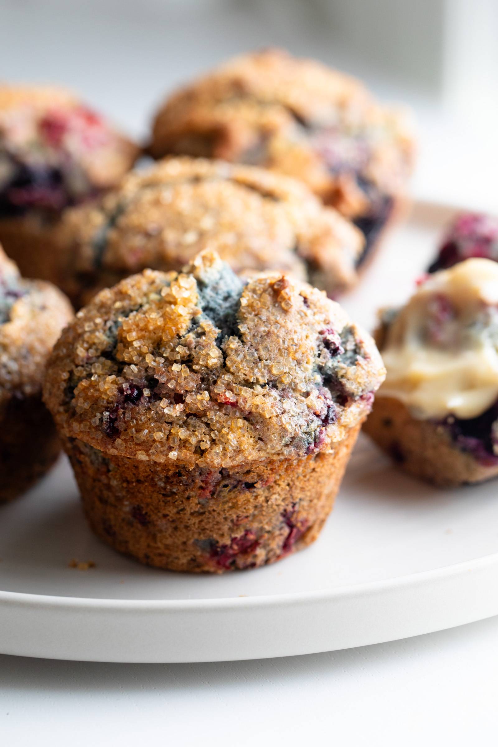 Mixed berry muffins on a plate with sugary tops.