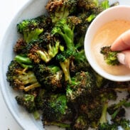 Air fryer broccoli on a plate with sauce in a bowl.