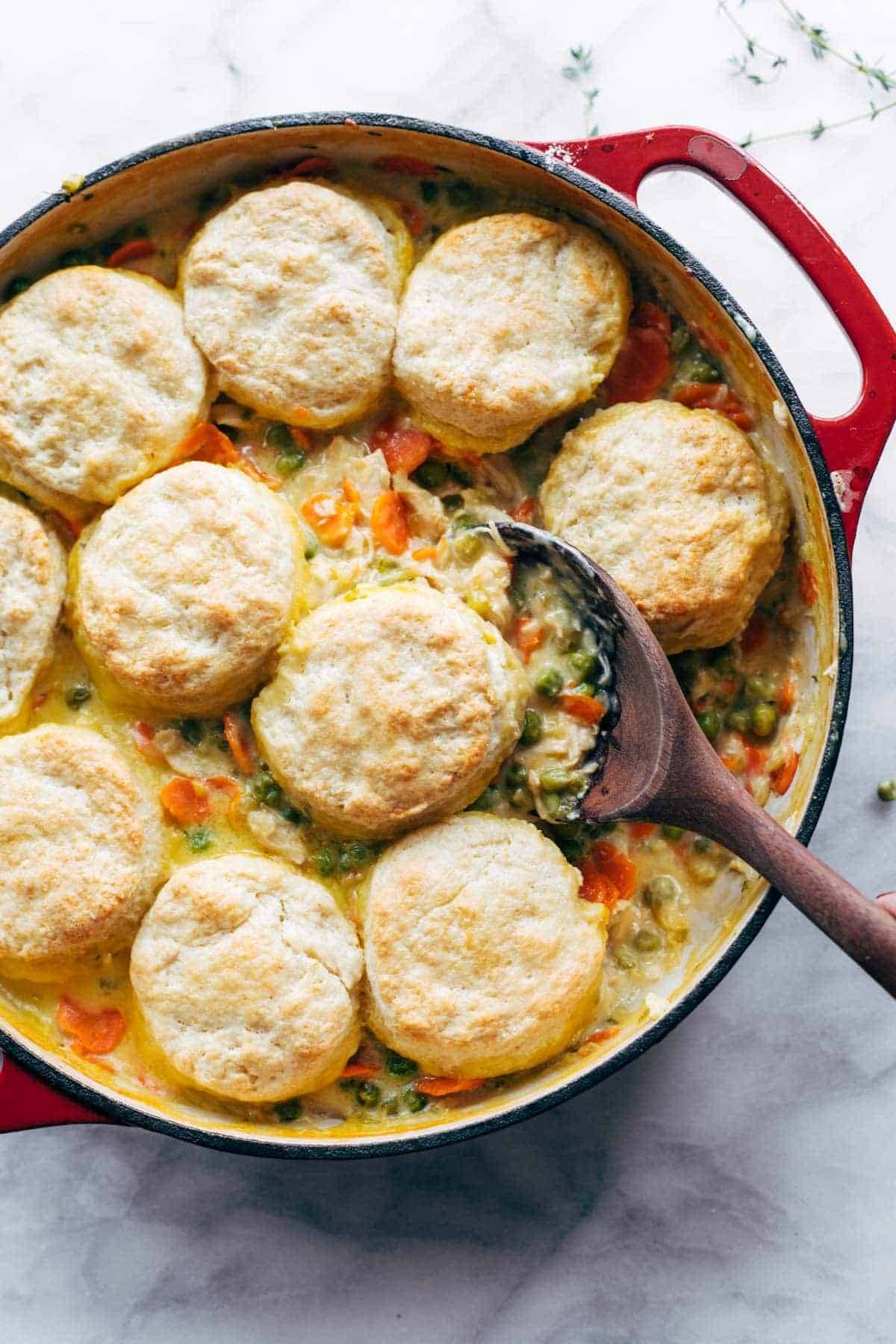 The Best Chicken Pot Pie with Biscuits in a big red pot with a wooden spoon.