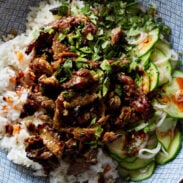 Black pepper beef in a bowl with rice and cucumber salad.