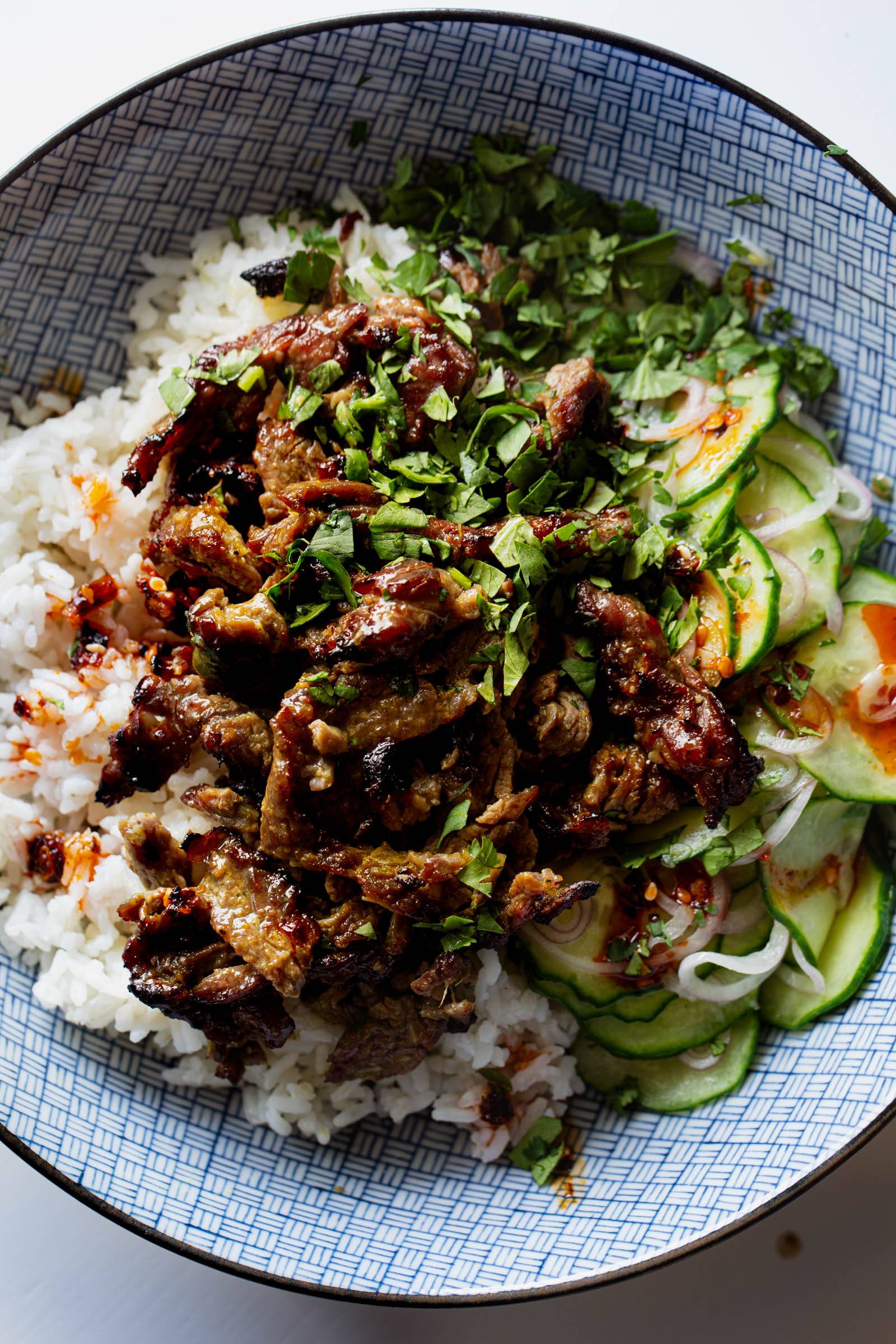 Crispy steak pieces in a bowl with rice, cucumber salad, and herbs.