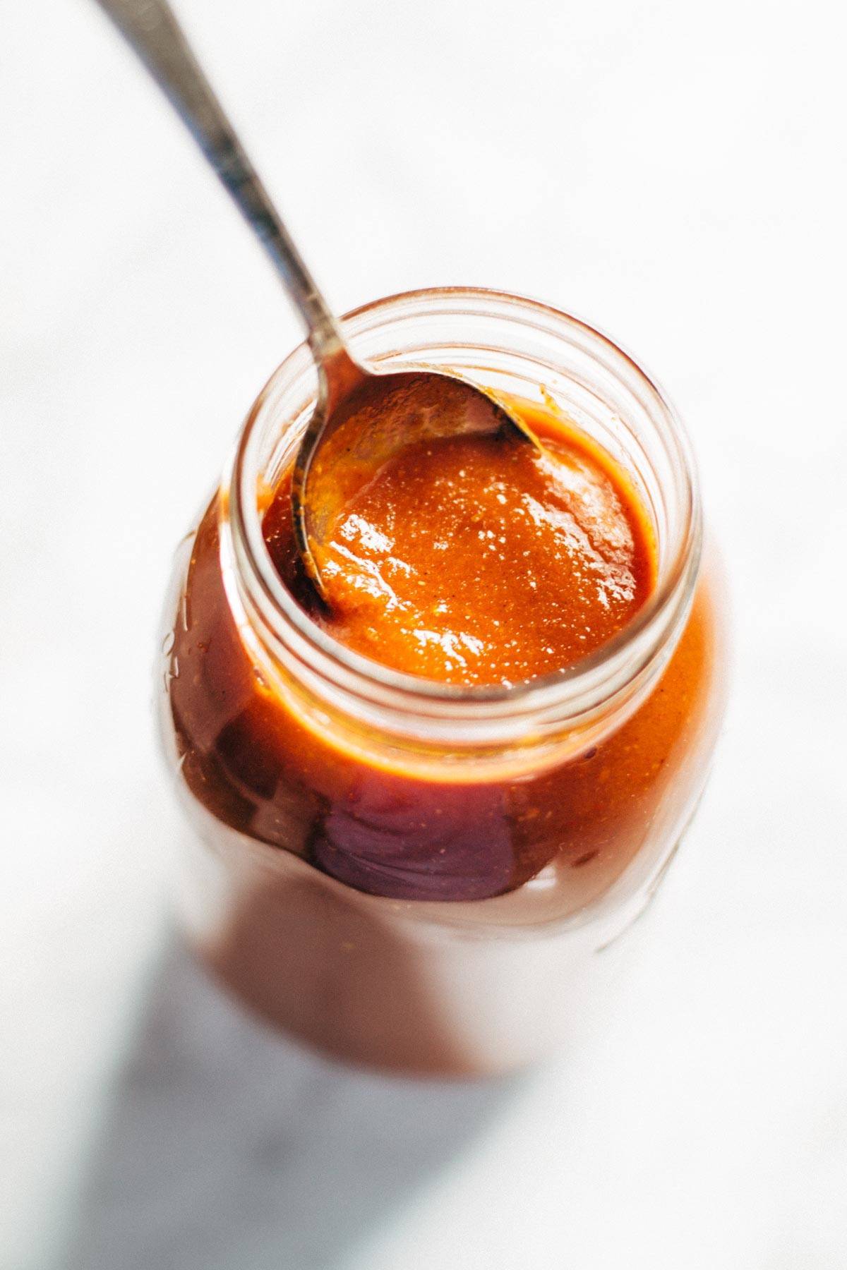 Enchilada sauce in a jar with a spoon.