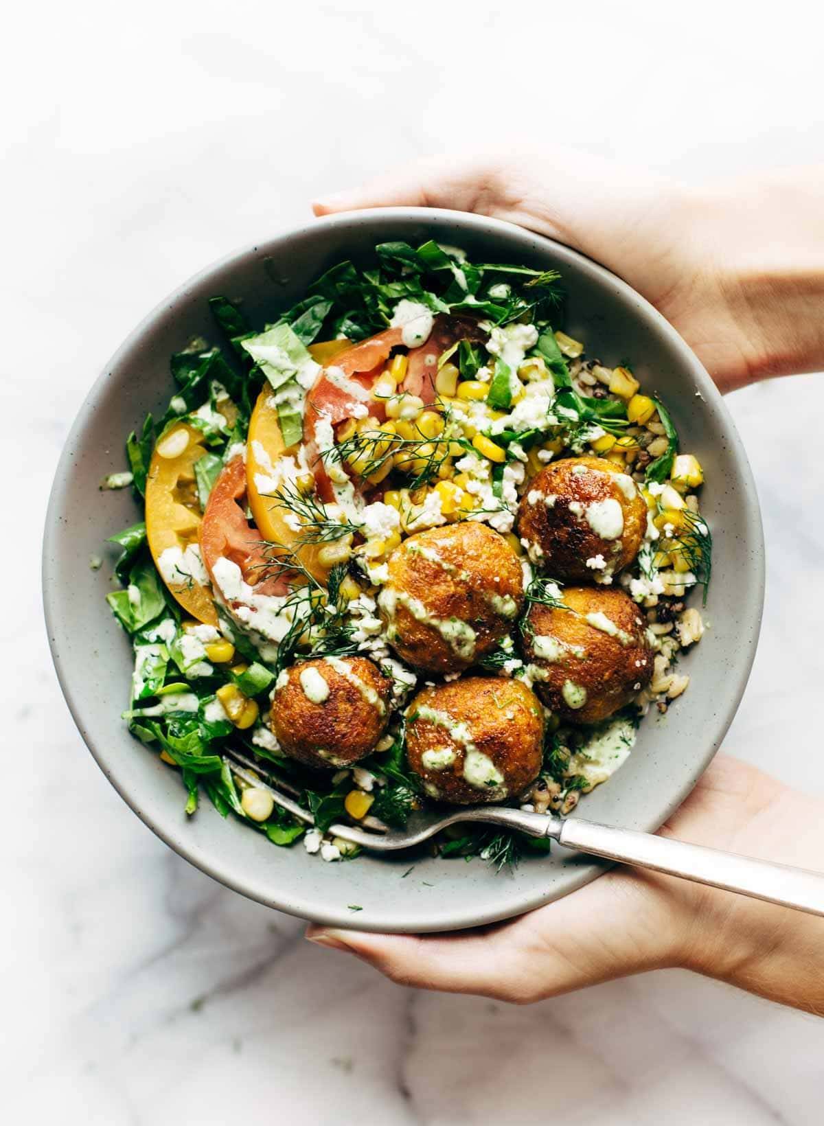 Hands holding Summer Bliss Bowls with Sweet Potato Falafel and Jalapeño Ranch. 
