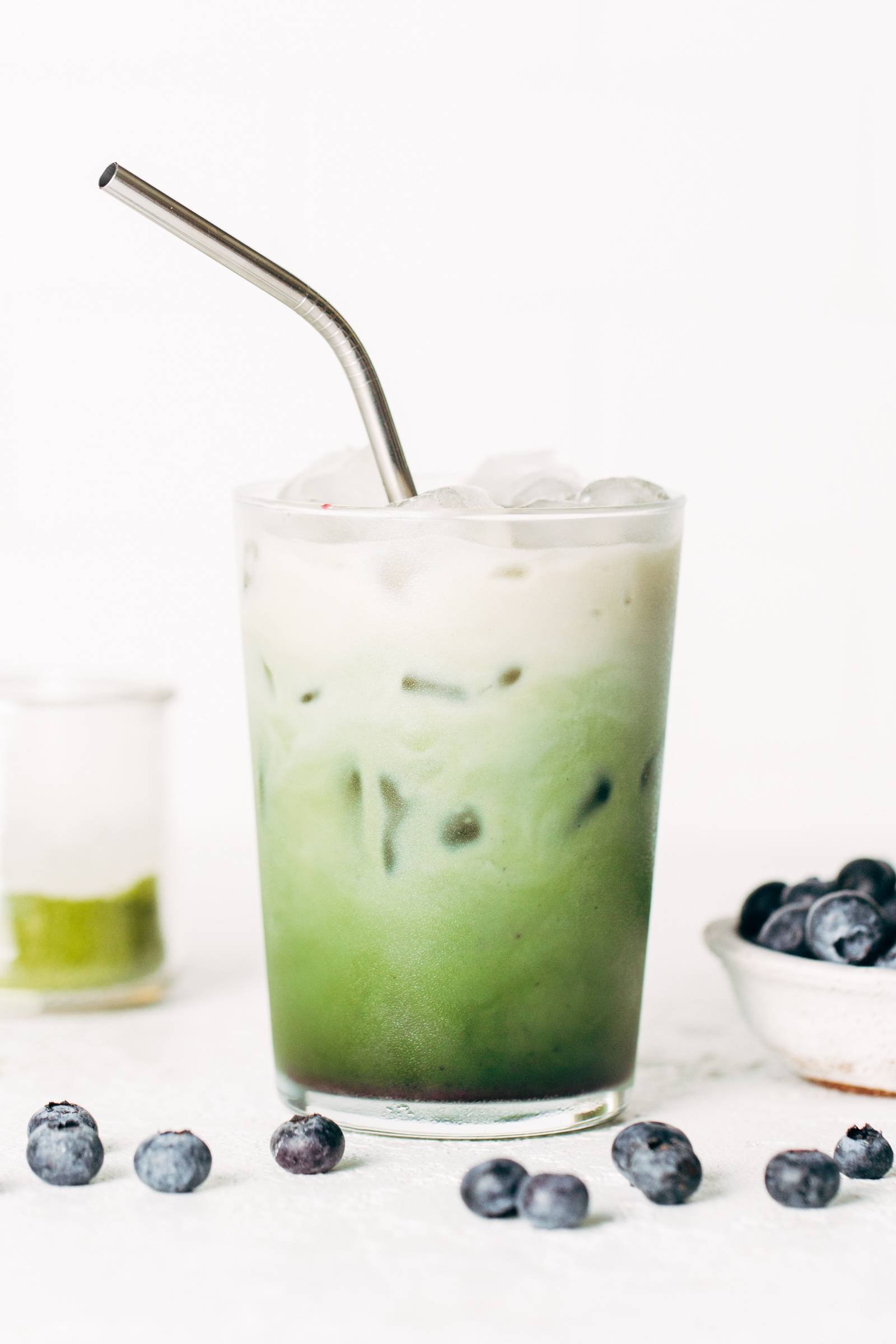 Blueberry matcha latte in a glass with a stainless steel straw