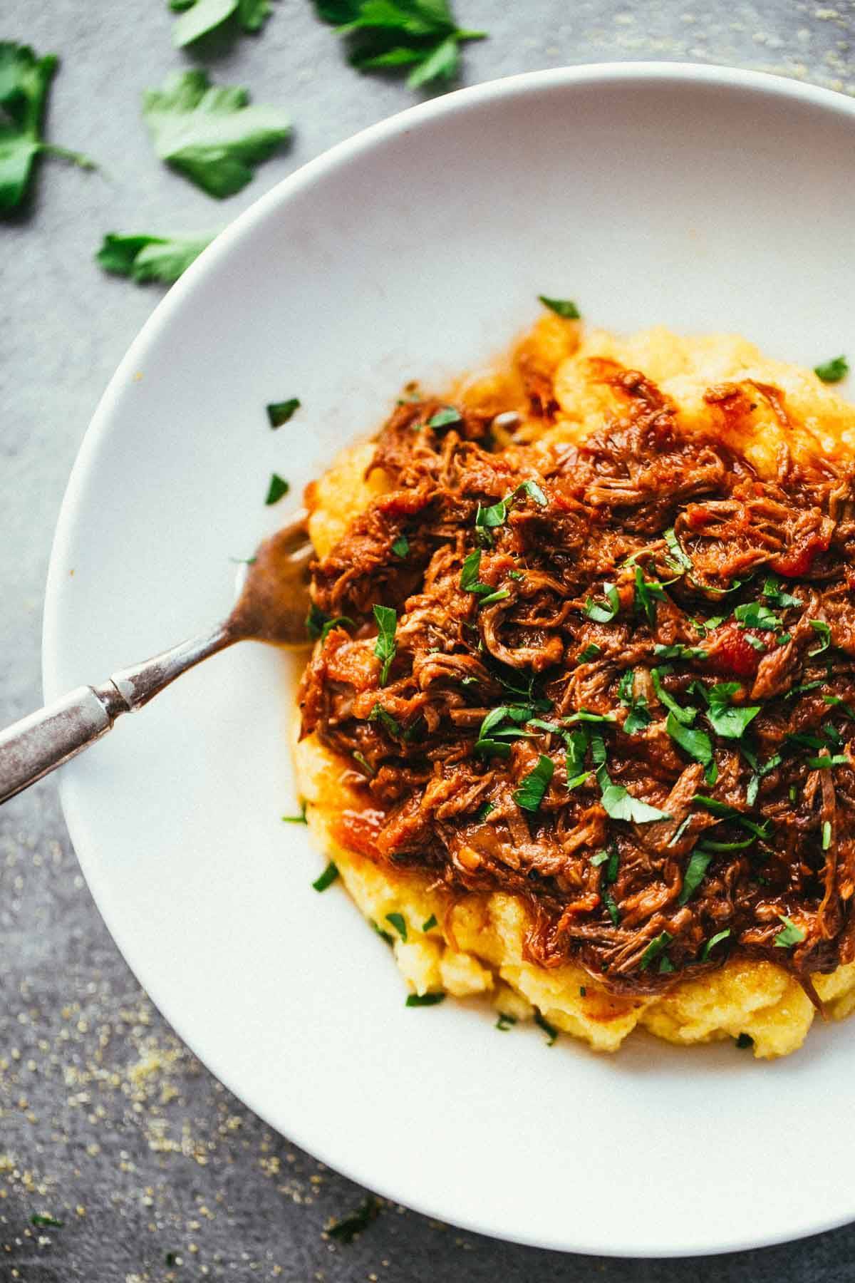 Crockpot Braised Beef Ragu with Polenta on a white plate with a fork.