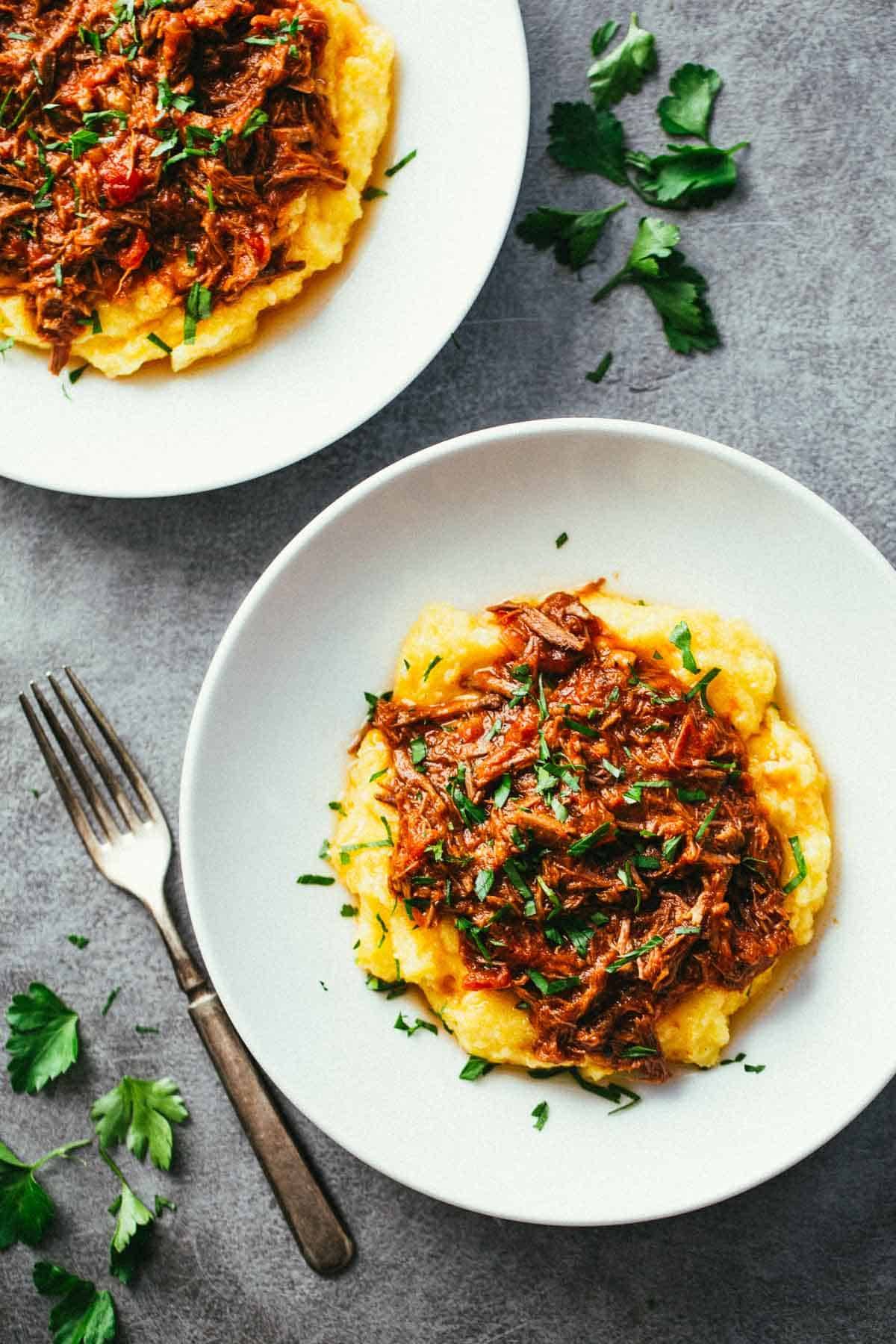 Crockpot Braised Beef Ragu with Polenta on two white plates.