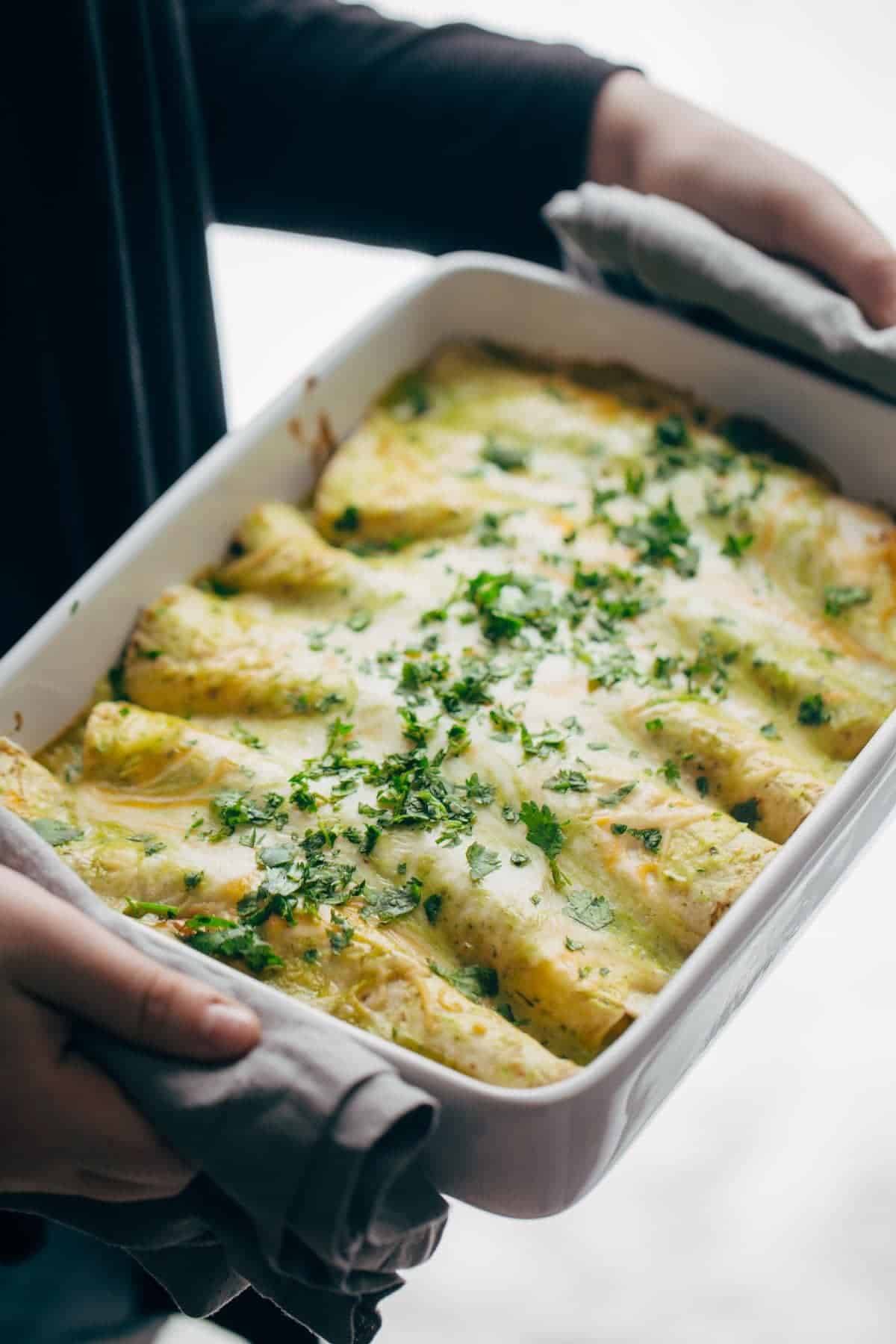 person holding a pan that contains enchiladas 