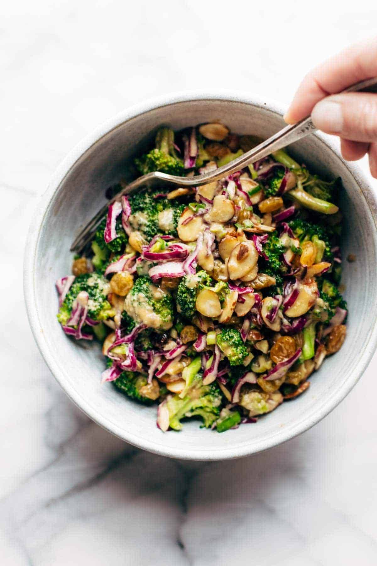 Broccoli salad in a bowl with a hand holding a fork.
