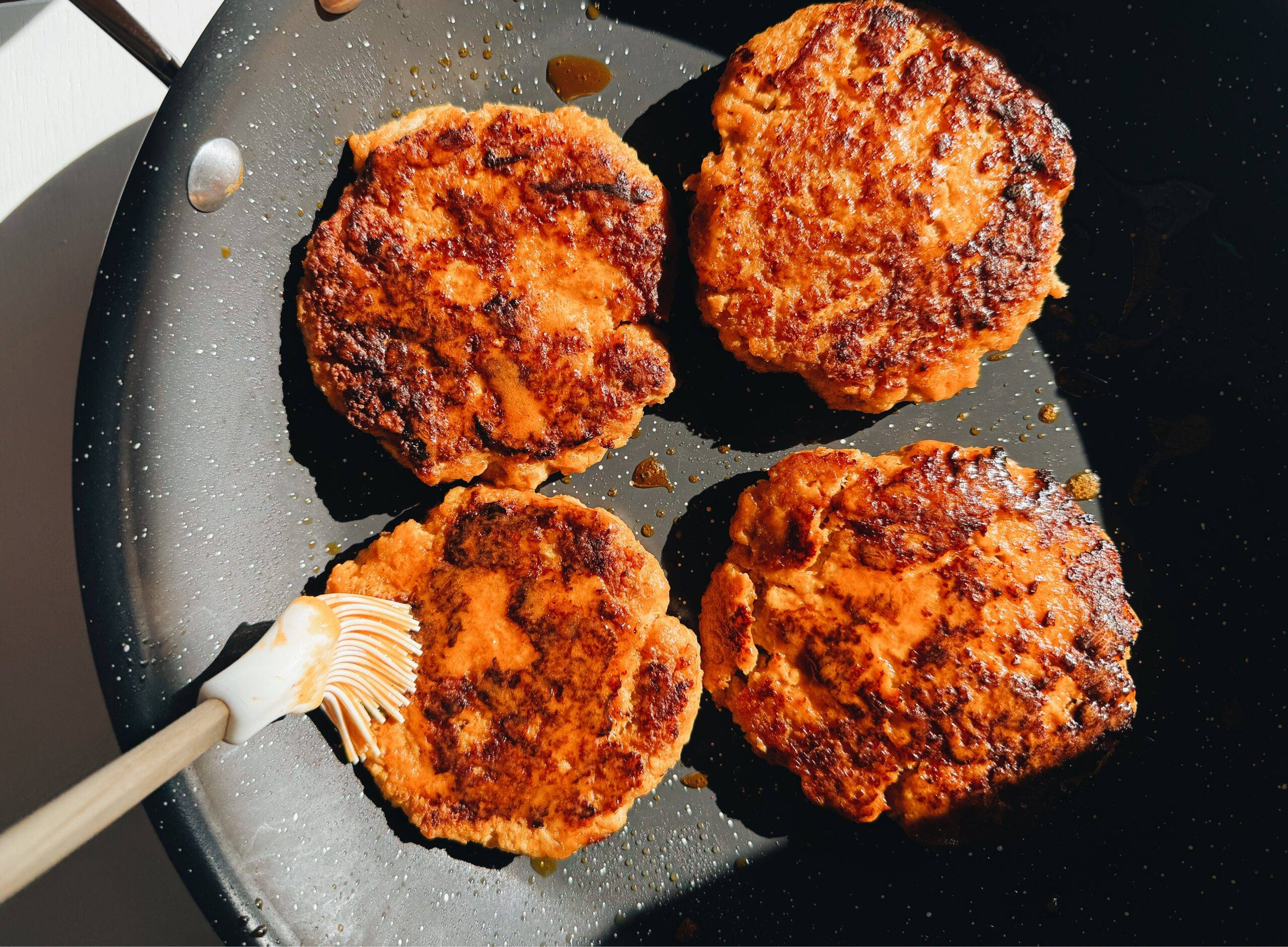 Brushing chicken burgers with buffalo sauce and butter.